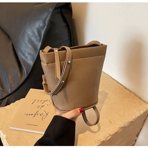 Détail du sac seau kaki avec clous argentés sur une surface en pierre beige en lumière