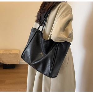 Close-up of black tote bag with wrinkled leather texture on shoulder of beige trench coat