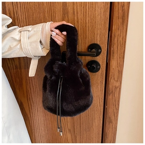 Détail d'un sac seau en fausse fourrure noire avec cordon accroché à une poignée en bois