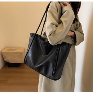 Detail of a large black tote bag in pleated faux leather worn with a trench coat