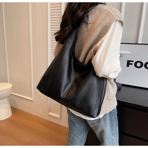 Detail shot of a black pebbled leather hobo tote bag worn on a woman's shoulder