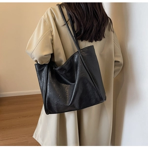 Detail of a large black faux leather tote bag showing natural textured finish and dual straps