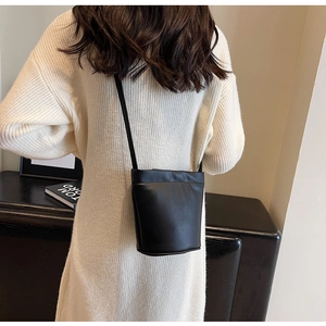 Vue arrière d'un mannequin portant un sac seau minimaliste noir sur une robe en tricot blanche