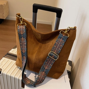 Retro brown suede tote bag with vintage patterned wide strap on a white suitcase