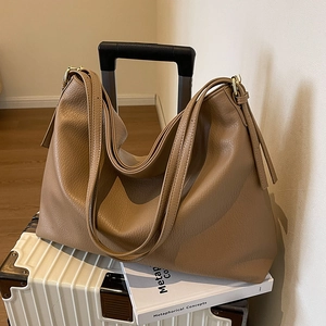 Brown lychee leather tote bag with long straps placed on a white suitcase and book