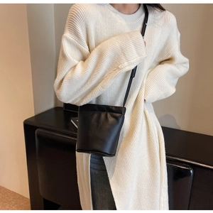 Gros plan d'un sac seau en cuir noir mat porté en bandoulière sur un pull en maille blanc