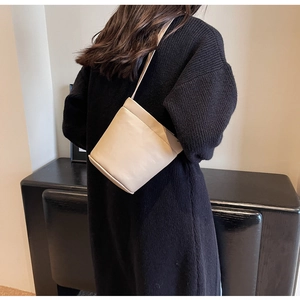 Gros plan d'un sac seau en cuir blanc crème porté par un mannequin en pull noir élégant