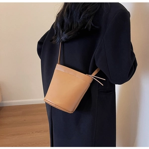 Sac seau marron en similicuir porté en bandoulière par un mannequin en manteau noir