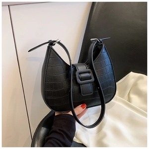 Detail of black crocodile-embossed half-moon bag with large buckle and adjustable strap