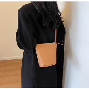Vue de dos d'un mannequin portant un sac seau en cuir marron caramel avec bandoulière