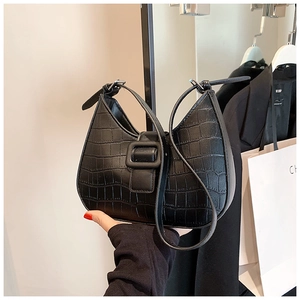 Detail of black crocodile texture saddle bag with square buckle in a retail setting