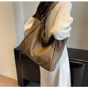 Brown oversized tote bag in pleated faux leather worn by a model in a modern interior