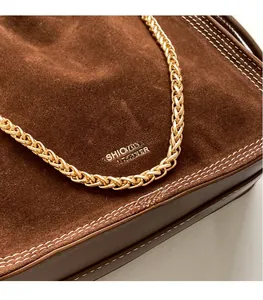 Close-up of brown suede bag with white stitching and gold chain strap detail