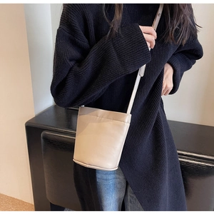 Gros plan d'un mini sac seau beige en cuir avec fine bandoulière sur un pull noir