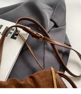 Detail of adjustable leather strap with white stitching and gold chain on suede bucket bag