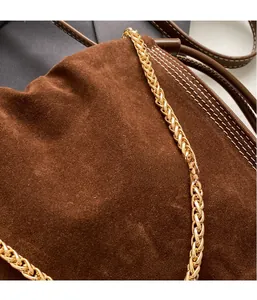Close-up of matte suede bucket bag with white contrast stitching and gold chain