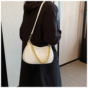Détail d'un sac demi-lune blanc plissé avec chaîne dorée sur un manteau noir