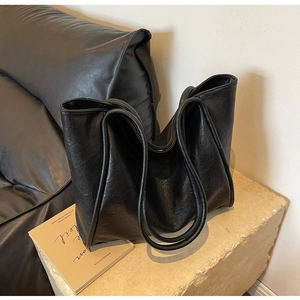 Close-up of a large black leather tote bag with crinkled texture on a stone surface