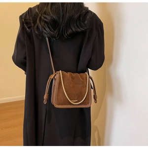 Detail of brown vintage bucket bag showing suede texture, gold lettering, and chain strap