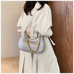 Détail du sac demi-lune plissé argenté avec chaîne dorée porté sur un trench-coat