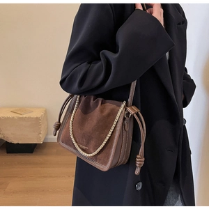 Detail of dark brown suede bucket bag featuring contrast stitching and gold chain strap