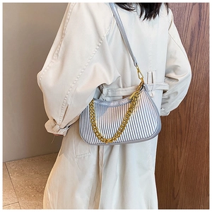 Détail du sac croissant argenté plissé avec chaîne dorée sur un trench-coat