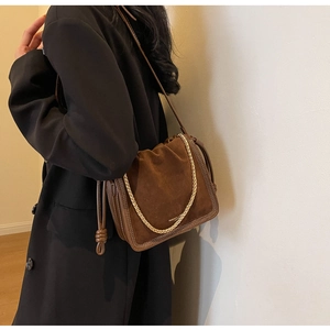 Detail of brown suede bucket bag featuring chunky gold chain and knot pendant detail