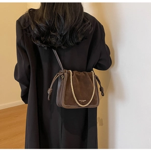 Detail of a brown suede bucket bag with gold chain strap shown on a model's shoulder