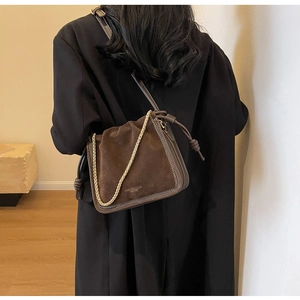 Detail of dark brown suede bucket bag with gold chain and leather drawstring knot