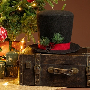 Detail of Christmas tree topper black top hat with red ribbon and pine cone on vintage case