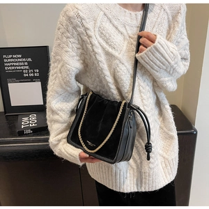 Detail of black crossbody bucket bag with mixed textures, stitching and chain strap