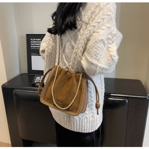 Detail of brown suede bucket bag with gold chain strap and drawstring knot design