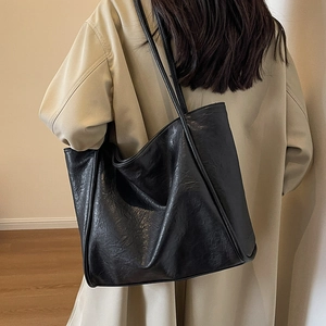 Large black leather tote bag for women worn over shoulder with minimalist beige coat