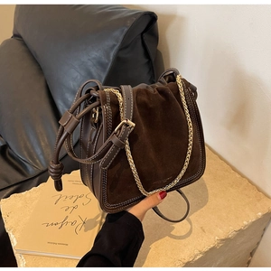 Detail of dark brown matte leather bucket bag with contrast stitching and gold chain