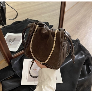 Detail of dark brown suede bucket bag featuring contrast stitching and gold chain strap
