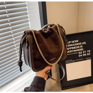 Detail of dark brown suede bucket bag with gold chain strap and stitching