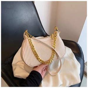 Détail du sac plissé crème avec chaîne dorée et texture en similicuir sur un siège chic