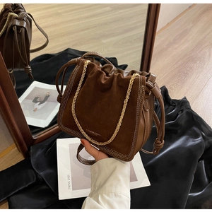 Detailed view of brown bucket bag showing suede splicing, white stitching and gold chain