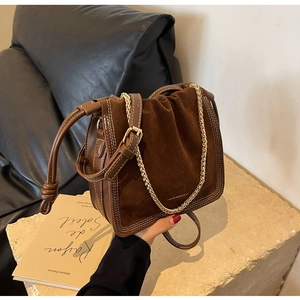 Detail of brown suede bucket bag with gold chain and contrast stitching on stone base