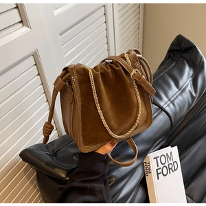 Detail of dark brown suede bucket bag featuring chunky gold chain and knot drawstring accents