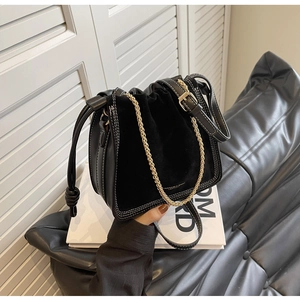 Detail of black matte leather bucket bag with white stitching and gold chain strap