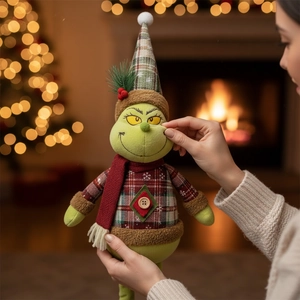 Close-up of Grinch plush in plaid sweater with Christmas tree bokeh background
