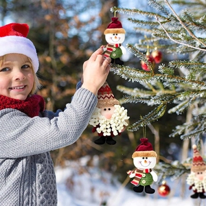Junge hängt Plüsch-Schneemann und Weihnachtsmann-Deko an einen verschneiten Baum