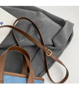 Detail of adjustable long shoulder strap with gold metal buckle on denim bucket bag