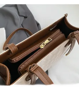 Detail of golden metal zipper and brown leather trim on beige quilted tote bag