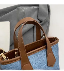 Close-up of blue denim bucket bag with brown leather handles and gold-tone hardware