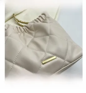 Detail view of beige quilted leather texture and elegant gold metal chain strap on bucket bag