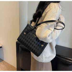 Detailed close-up of black quilted leather texture and gold logo on the tote bag