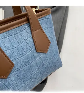 Close-up of blue crocodile pattern denim fabric with brown leather trim and gold hardware