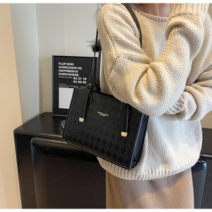 Detail of black quilted tote bag with gold hardware and leather logo on textured PU fabric